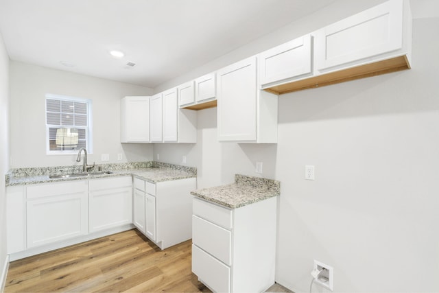 kitchen with light stone countertops, a sink, light wood-style floors, recessed lighting, and white cabinetry