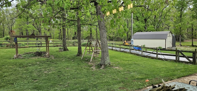 view of yard featuring fence, a forest view, an outdoor structure, and a storage shed