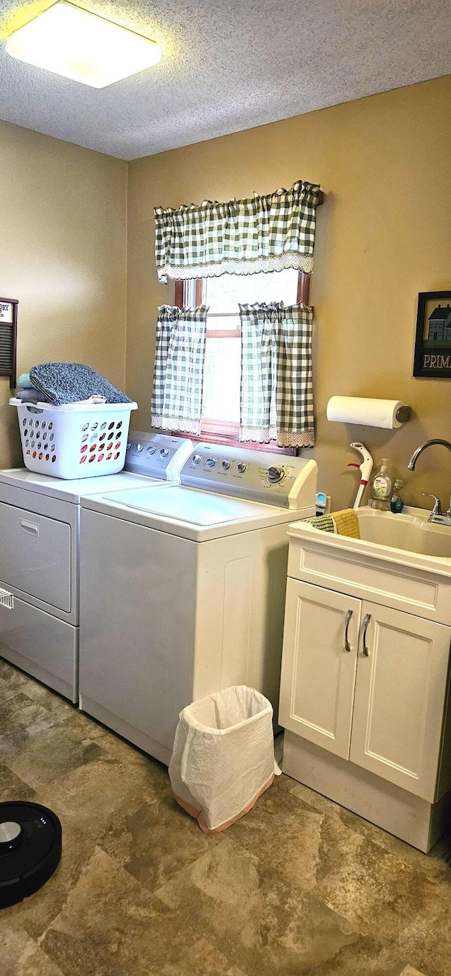 laundry area with a sink, a textured ceiling, cabinet space, and washer and clothes dryer