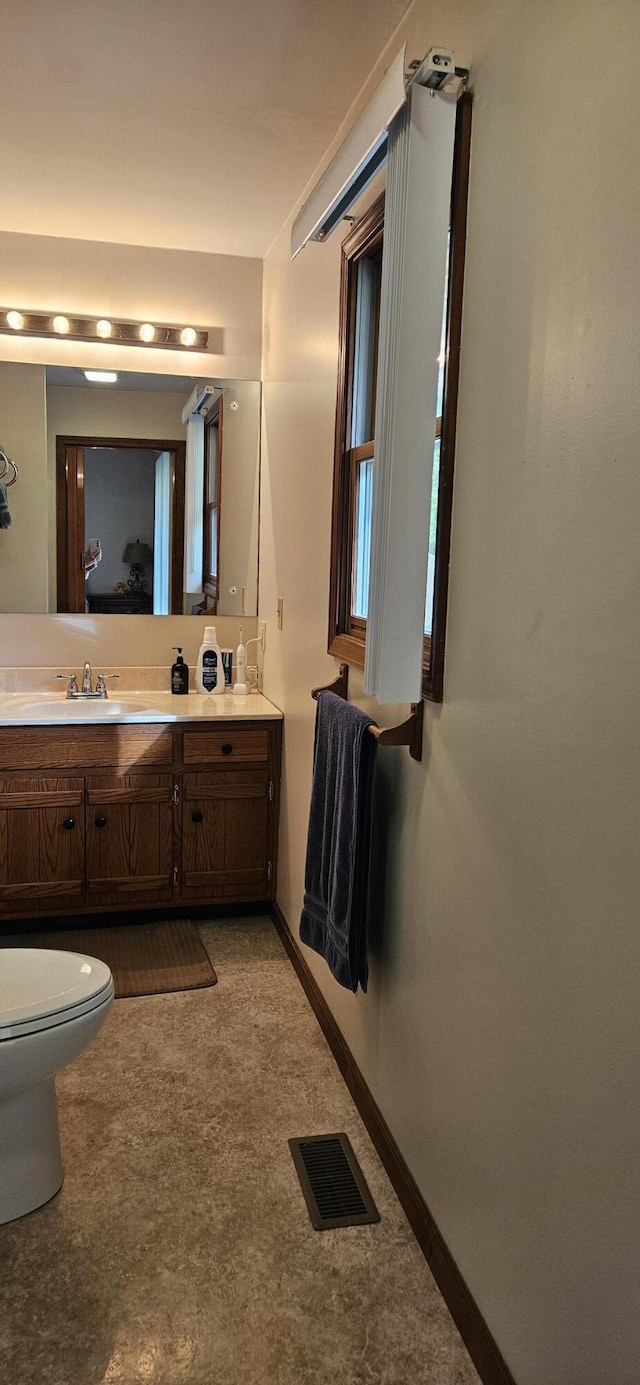 bathroom with visible vents, double vanity, toilet, baseboards, and a sink
