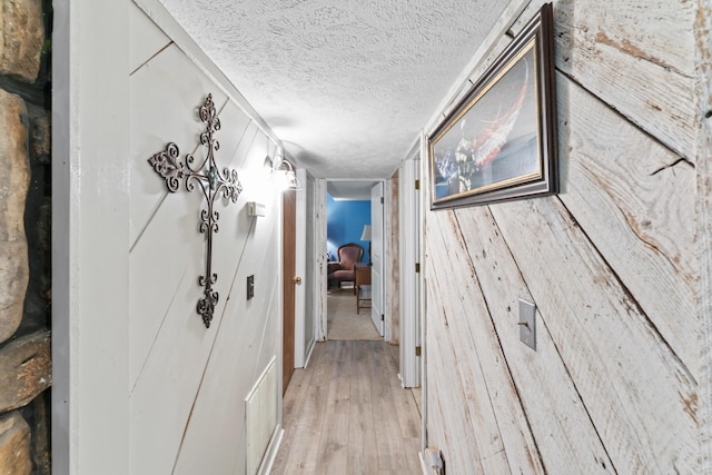 hallway featuring a textured ceiling, visible vents, and light wood-style flooring
