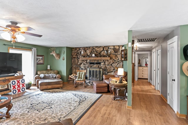 living room featuring a ceiling fan, a stone fireplace, visible vents, baseboards, and light wood finished floors