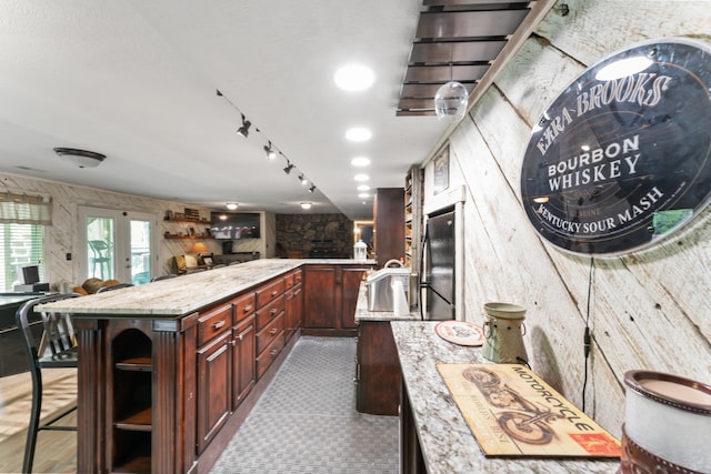 kitchen with light stone countertops, open shelves, a sink, wood walls, and open floor plan