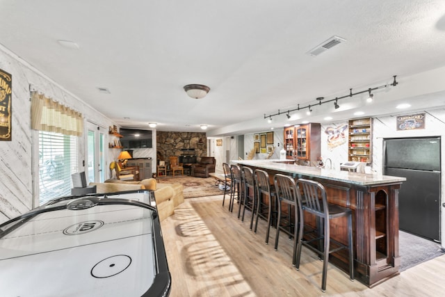 kitchen with visible vents, freestanding refrigerator, a breakfast bar, a stone fireplace, and light wood-type flooring