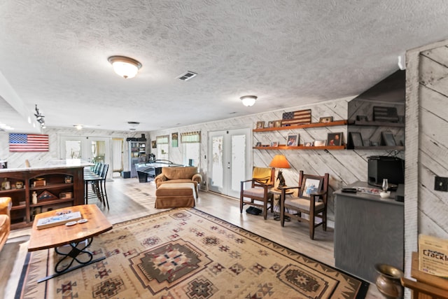 living room featuring french doors, a textured ceiling, wood finished floors, and visible vents