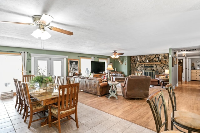 dining space with visible vents, a fireplace, ceiling fan, a textured ceiling, and light tile patterned floors