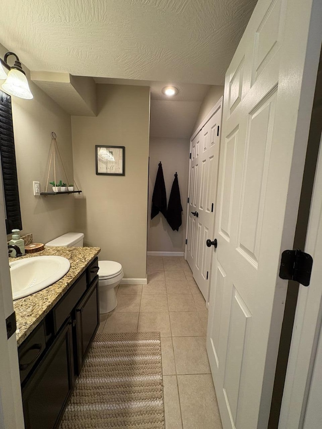 half bathroom featuring tile patterned flooring, vanity, toilet, a textured ceiling, and baseboards