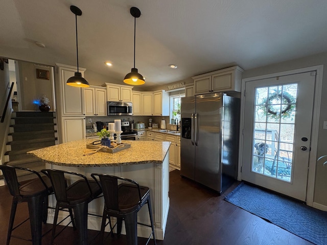 kitchen featuring hanging light fixtures, a sink, a center island, stainless steel appliances, and a kitchen bar