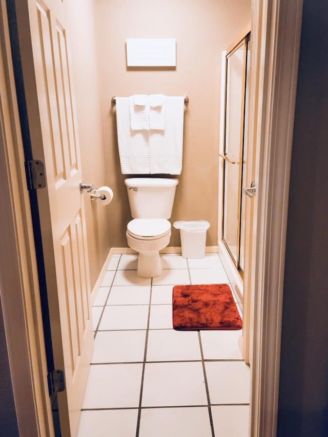 bathroom with tile patterned floors, baseboards, a stall shower, and toilet
