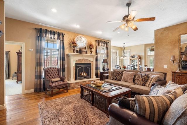living room featuring wood-type flooring, a ceiling fan, a warm lit fireplace, and a wealth of natural light