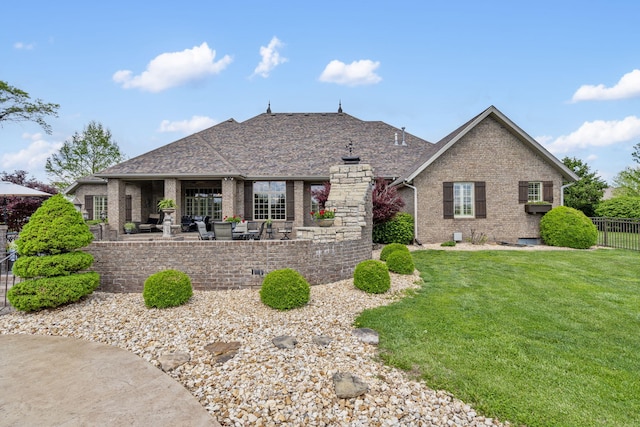 single story home with fence, a shingled roof, a front lawn, brick siding, and a patio