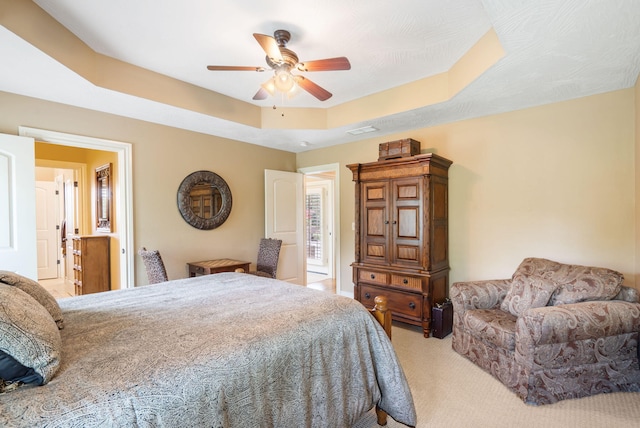 carpeted bedroom with a ceiling fan, a tray ceiling, and visible vents