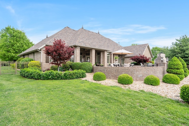 view of front facade featuring fence, a front yard, roof with shingles, and brick siding