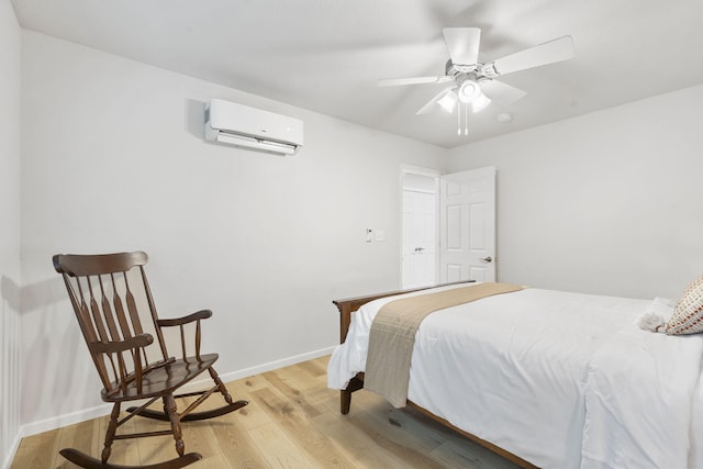 bedroom featuring a ceiling fan, baseboards, a wall unit AC, and light wood-type flooring