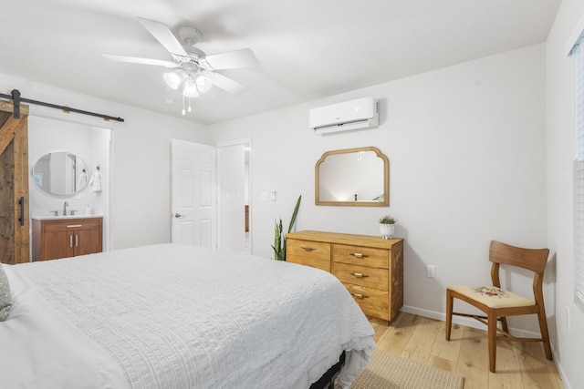 bedroom with a barn door, a wall mounted air conditioner, a sink, baseboards, and light wood-style flooring