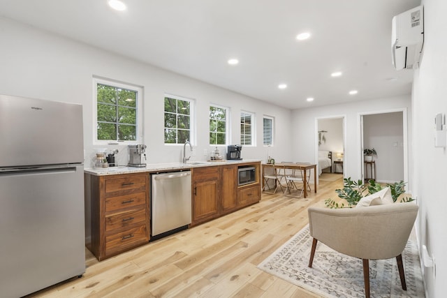 kitchen with an AC wall unit, light wood-type flooring, brown cabinets, a sink, and stainless steel appliances