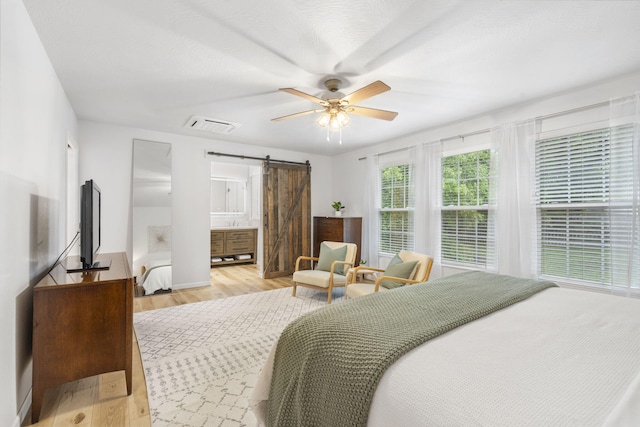 bedroom with ceiling fan, visible vents, a barn door, baseboards, and light wood-style flooring