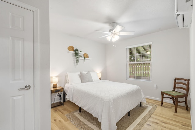 bedroom with light wood-style floors, a wall mounted air conditioner, baseboards, and a ceiling fan