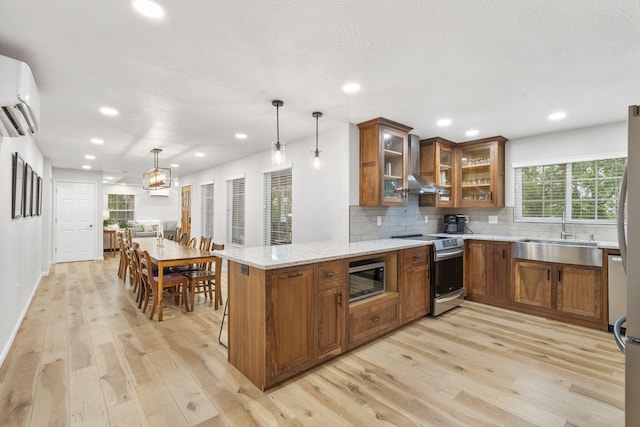 kitchen featuring brown cabinetry, a peninsula, light stone counters, a sink, and stainless steel appliances
