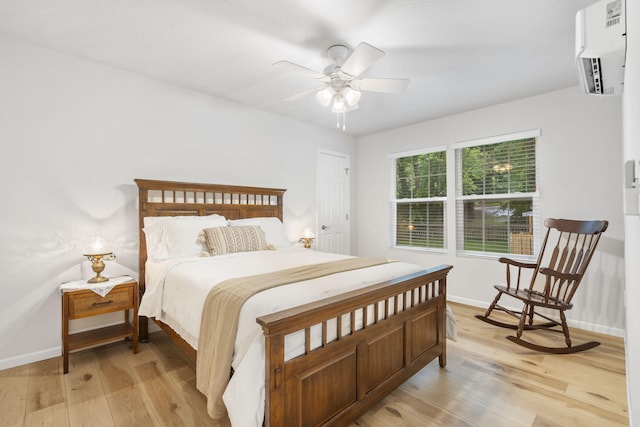 bedroom featuring an AC wall unit, a ceiling fan, light wood finished floors, and baseboards