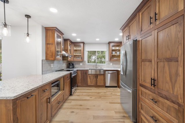 kitchen with light wood-style floors, brown cabinets, light stone counters, a sink, and appliances with stainless steel finishes