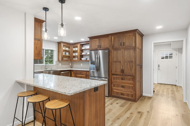 kitchen with brown cabinetry, appliances with stainless steel finishes, light stone countertops, a peninsula, and light wood finished floors