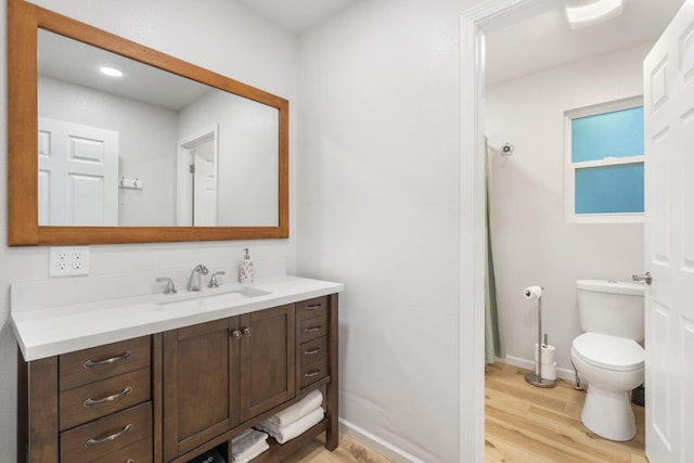 bathroom featuring toilet, baseboards, wood finished floors, and vanity