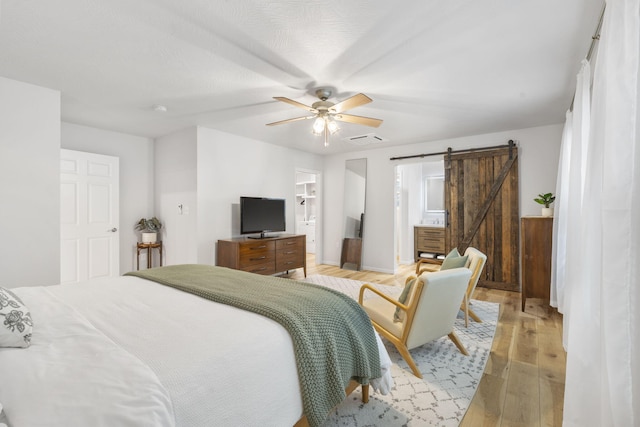 bedroom with ceiling fan, a barn door, light wood-style flooring, ensuite bathroom, and visible vents