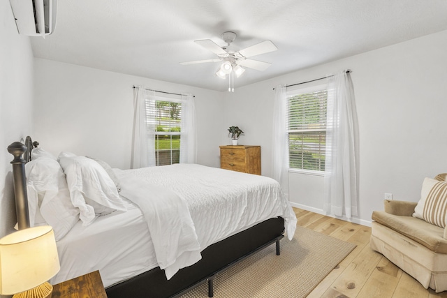bedroom with light wood-style floors, baseboards, ceiling fan, and an AC wall unit