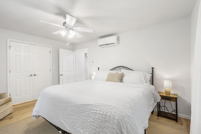 bedroom with ceiling fan, baseboards, light wood-type flooring, a wall mounted AC, and a closet