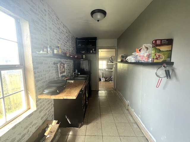 kitchen featuring light tile patterned floors, baseboards, butcher block counters, and a sink