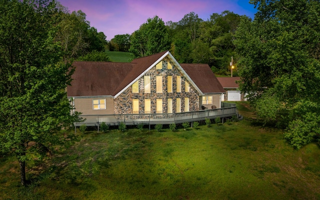 back of house at dusk featuring a yard and stone siding