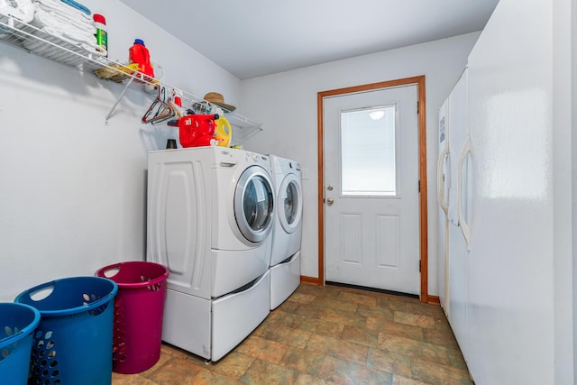 washroom featuring stone finish floor, baseboards, laundry area, and washing machine and clothes dryer