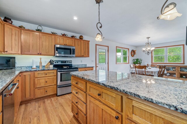 kitchen featuring light stone countertops, a notable chandelier, appliances with stainless steel finishes, light wood finished floors, and decorative light fixtures