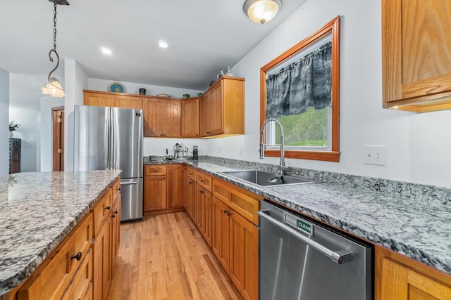 kitchen featuring light stone counters, a sink, light wood finished floors, hanging light fixtures, and stainless steel appliances