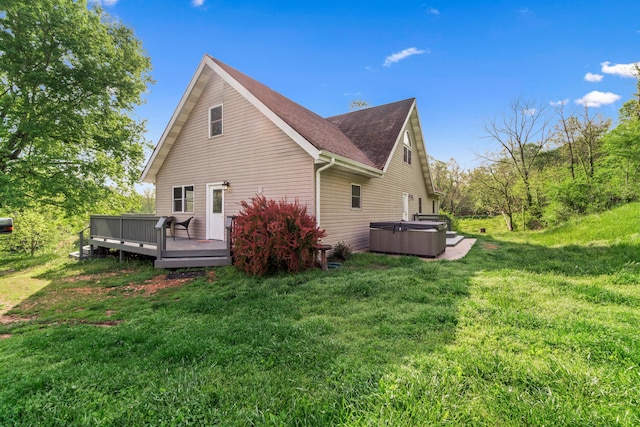 rear view of property featuring a shingled roof, a hot tub, a wooden deck, and a yard