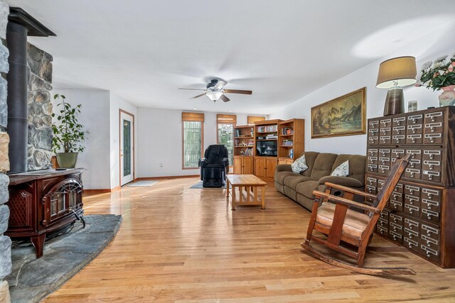 living room with light wood-style floors, ceiling fan, and a wood stove