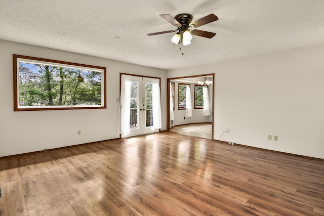 unfurnished room with french doors, baseboards, wood finished floors, and ceiling fan with notable chandelier