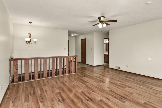 spare room with visible vents, baseboards, ceiling fan with notable chandelier, and wood finished floors