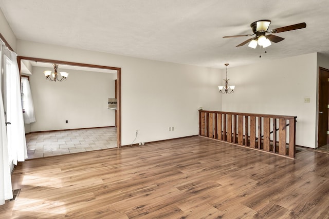 spare room with baseboards, ceiling fan with notable chandelier, and wood finished floors