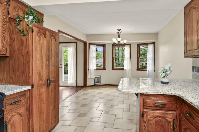 kitchen with brown cabinetry, a peninsula, a notable chandelier, and light stone countertops