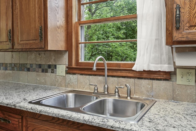 kitchen with brown cabinetry, a sink, tasteful backsplash, and light countertops