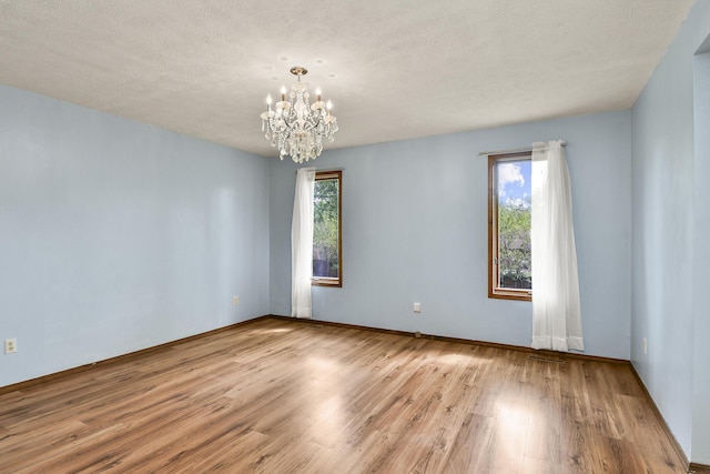 spare room featuring baseboards, a textured ceiling, wood finished floors, and a notable chandelier