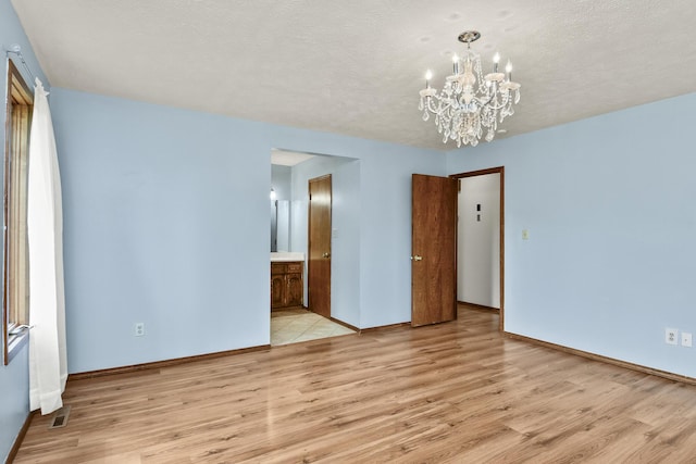 empty room featuring an inviting chandelier, baseboards, and light wood-type flooring