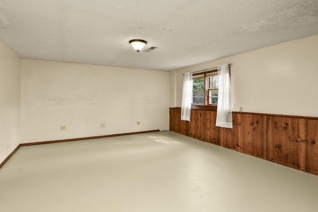 spare room featuring a textured ceiling, visible vents, a wainscoted wall, concrete floors, and wooden walls
