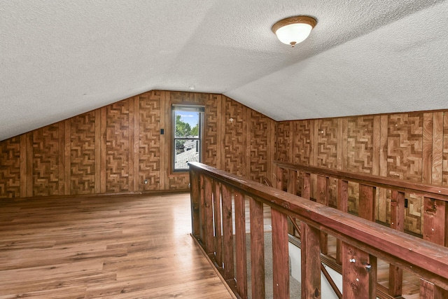 bonus room with light wood-style floors, a textured ceiling, vaulted ceiling, and wooden walls