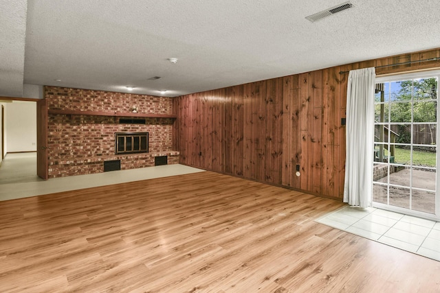 unfurnished living room featuring a brick fireplace, a textured ceiling, visible vents, and wood finished floors