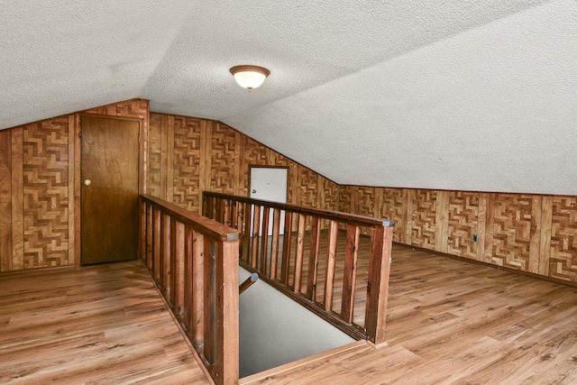 bonus room with wooden walls, light wood-type flooring, a textured ceiling, and lofted ceiling