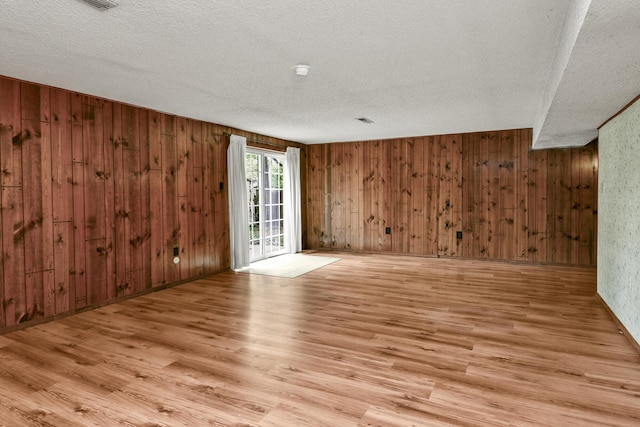 spare room featuring wooden walls, a textured ceiling, and light wood finished floors