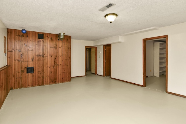 finished below grade area featuring visible vents, wood walls, baseboards, and a textured ceiling